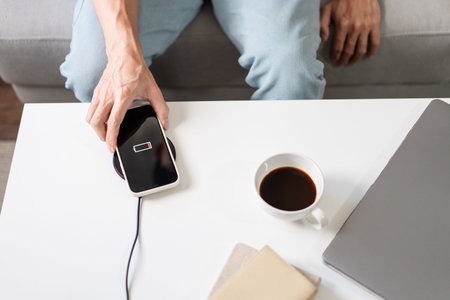 Technology Concept. A person with his light blue jeans sitting on the couch and trying to charge his...
