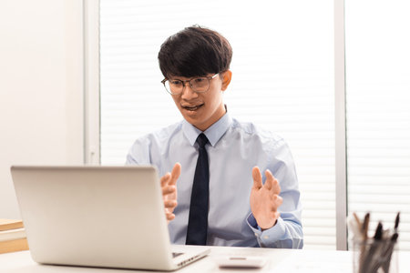 Working Man Conept The man with glasses sitting at his desk, smiling, and explaining something through the screen of the notebook.の写真素材