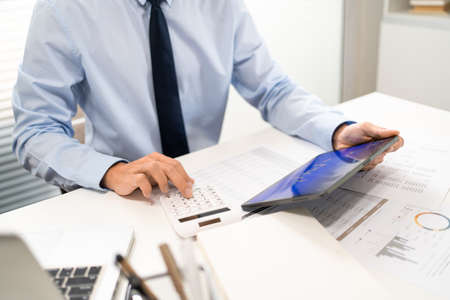 Working Man Conept The office man holding tablet and pressing the calculator while sitting in the office.の写真素材