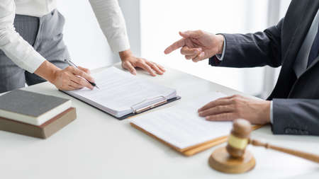 law concept The barrister helper standing, holding a pen in his hand, and reading the term that seems to be confused for him to his boss.の写真素材