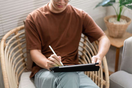 Technology Concept The young man who is sitting on the chair holding his tablet and noting something on it.の写真素材