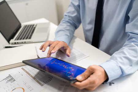 Working Man Conept The male employee sitting at his desk, holding a tablet, and touching the screen...