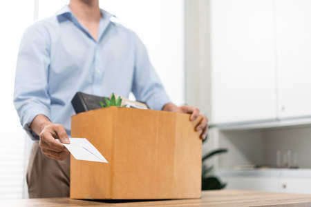 Resignation Concept The male officer standing, putting his box of his belongs on the desk and...