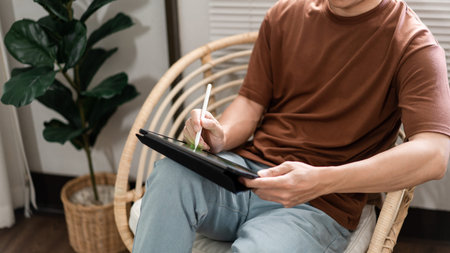Technology Concept. The young man who is sitting on the chair holding his tablet and noting...