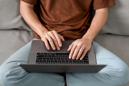 Technology Concept The male who is wearing casual clothes sitting on the sofa, resting his notebook on his lap and doing his work.の写真素材