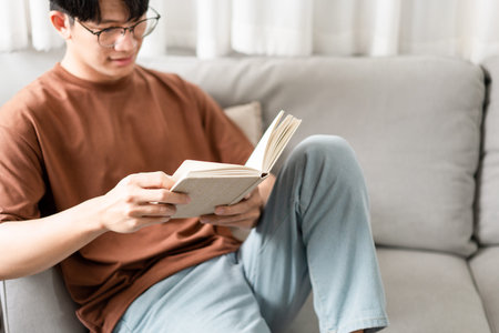 Technology Concept The male with his glasses sitting on the grey sofa, leaning his back on it, and...