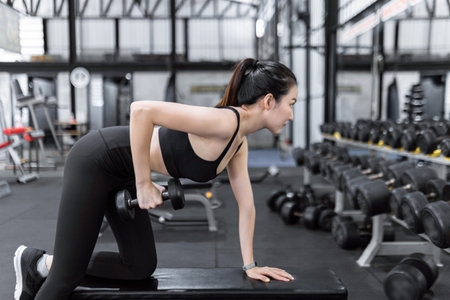 exercise concept The female exercise beginner doing dumbbell workout by resting her left knee and...