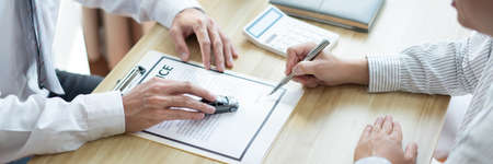 Insurance concept the customer signing his name on the contract while the dealer giving more details.の写真素材