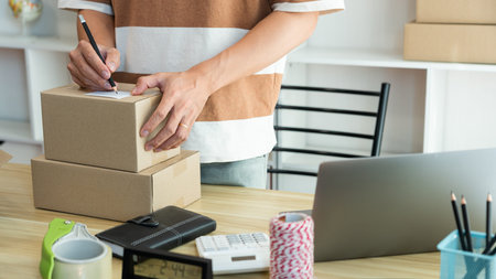 Online shopping concept the seller writing his customerâ€™s address on the parcel and being...