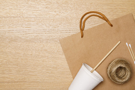 Eco friendly concept, Paper eco bag and jute rope with coffee cup and straws on wooden background.