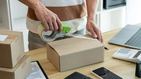 Online shopping concept the shop seller sealing the parcel of his goods on the desk.の写真素材