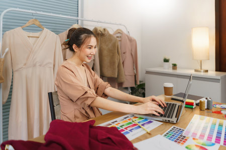 Fashion design concept, Asian female designer use laptop to relax after make to sewing clothes.の写真素材