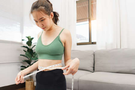 Healthy and weight loss concept, Young Asian woman use tape measure to measuring her waist size.の写真素材