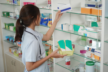 Medicine and health concept, Female pharmacist is taking medicine boxes from shelves into basket.の写真素材
