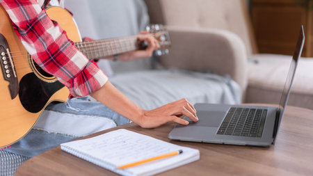 Guitar and singer concept, Young asian woman playing acoustic guitar while learning music on laptop.の写真素材