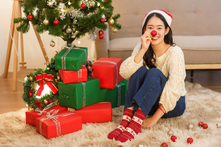 Christmas concept, Young asian woman in santa hat smiling and holding red ball to covering nose.の写真素材
