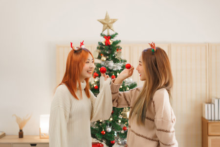 Christmas decoration concept, Two women wears reindeer horns and holds red ball with happiness.の写真素材