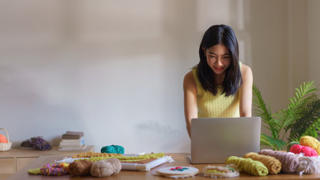 Hand embroidery concept, Women working on laptop and making handicraft embroidery with punch needle.の写真素材