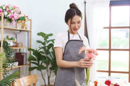 Flower shop concept, Female florist arrange pink gerbera and colorful flower in vase with happiness.の写真素材