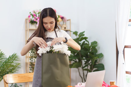 Florist concept, Female florist arranging chrysanthemum flower bouquet in shopping bag at shop.の写真素材