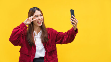 Women doing v sign gesture and selfie on smartphone with empty space on isolated yellow background.の写真素材