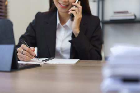 Work of secretary concept, Female secretary talks on phone with boss and taking notes in notebook.の素材