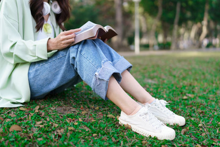 Women in headphone around neck and sitting on the grass to reading a book after cycling in the park.の写真素材