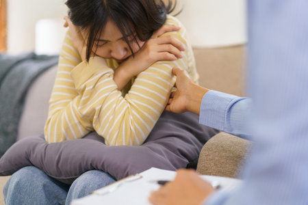 Female psychologist talking and comforting depressed patient while having session therapy in clinic.