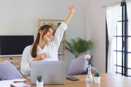 Relaxing time concept, Woman drinks coffee and arms stretching after tired of work at home office.の写真素材