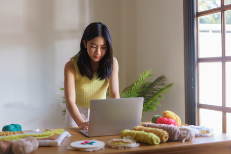 Hand embroidery concept, Women working on laptop and making handicraft embroidery with punch needle.の写真素材
