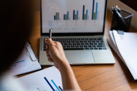 Close up hands of businessman reads document and pointing financial data on screen laptop with pen.の写真素材
