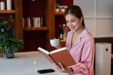 Female entrepreneur drinking coffee and reading a book with happiness to relaxation in home office.