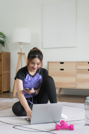 Young asian woman listening music and watching fitness video to preparing doing exercise at home.の写真素材