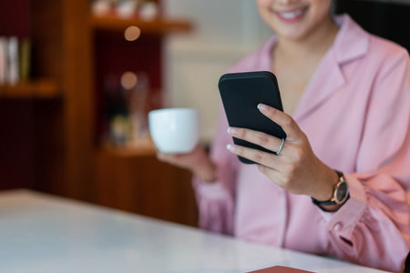 Businesswoman drinks coffee and read data on smartphone to analysis business project in home office.の写真素材