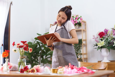 Flower shop concept, Female florist holds phone between face and shoulder to talking with customer.の写真素材