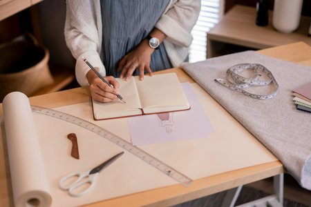 Asian tailor women creative and designing new fashion collection while drawing sketch in notebook.