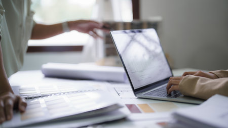 Female architects explain building model and interior design to partner while typing data on laptop.の写真素材