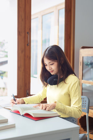 Education and literacy concept, College student girl reading textbook and taking notes in library.の写真素材
