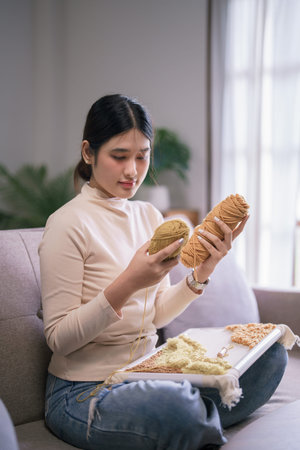 Young asian woman holding yarn to embroidery craft on fabric with punch needle in hobby lifestyle.