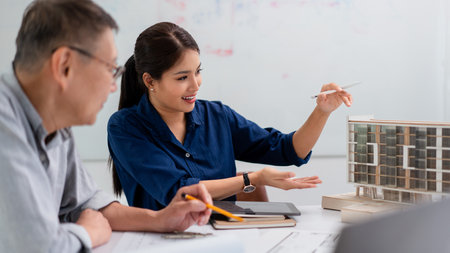 Female architect explaining architectural model of building and plan of project to senior partner.の写真素材