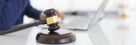 Lawyer woman typing business contract and law agreement on laptop with wooden judge gavel on desk.