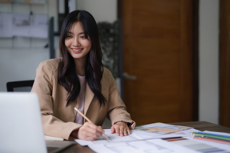 Female architect reading data on laptop to designing interior building and drawing on blueprint.の写真素材