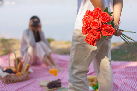 Young man holding rose bouquet behind his back and posing for girlfriend to taking photo on camera.の写真素材