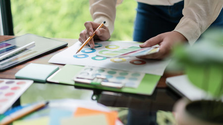 Creative graphic designer holding color swatch to comparing color on document for designing project.