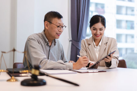 Female lawyer explains term and legal agreement while senior businessman signing contract on tablet.の写真素材