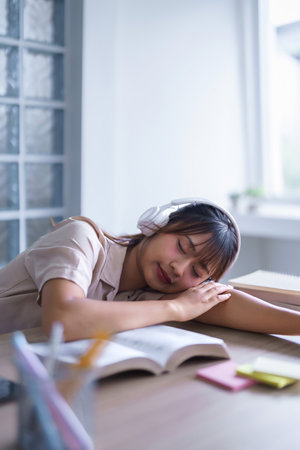 Young asian student in casual clothes wear headphones to listening music and sleep to resting on desk after reading a book and studying education knowledge to doing homework assignments in university.の写真素材