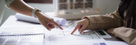 Two female architect discussion and inspection interior designing and building project on blueprint.