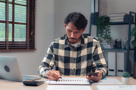 Businessman use smartphone and taking notes on paper while checking financial and accounting report.の写真素材