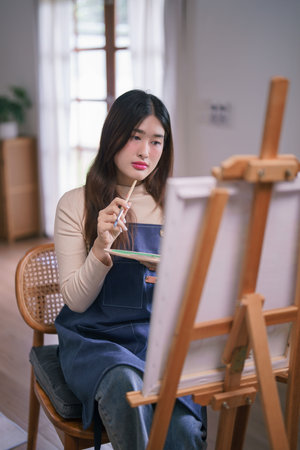 Young asian female artist sitting front of canvas and thinking idea to drawing and painting artwork.の写真素材