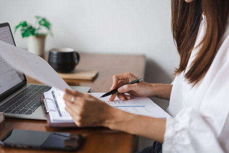 Businesswomen reading data on laptop and checking finance document while working in outside office.の写真素材